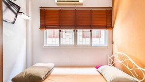 A single bed with a metal frame, a window with wooden blinds, and an air conditioning unit above the window. - 1137 Hostel (Bangkok)