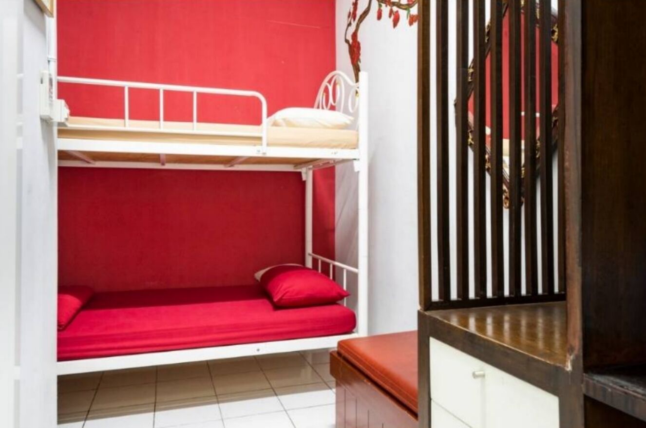 A bunk bed room with red bedding and a wooden bench.