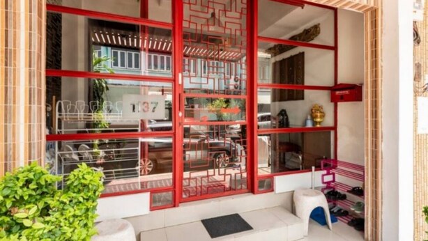 A building with a red-framed entrance, a visible number '137', and a small outdoor seating area with a stool. - 1137 Hostel (Bangkok)