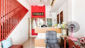 A reception area with a red staircase, a reception desk, a grey chair, a pink fan, and a clock on the wall. - 1137 Hostel (Bangkok)
