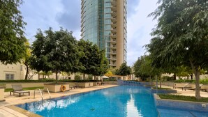 A swimming pool with lounge chairs, trees, and a tall building in the background. - Exclusive Duplex Villa w Panoramic Terrace Overlooking Burj Khalifa (Dubai)