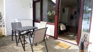 Eine Terrasse im Freien mit Tisch und Stühlen, eine Glasschiebetür, die zu einem Raum führt, und eine kleine Fußmatte.