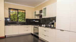 Una cocina con armarios blancos, encimera negra y ventana con vistas a zonas verdes.