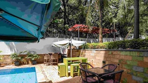 Un área junto a la piscina con piscina, sillas y una mesa bajo una pérgola.
