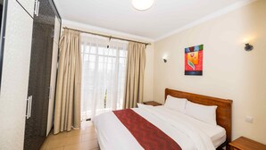 Habitación de hotel con una cama grande, cabecera de madera, mesita de noche, armario y una ventana con cortinas.