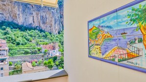 Vista desde un balcón sobre un pueblo costero, un acantilado y un mural colorido que representa una escena marinera.