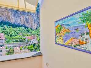 Vista desde un balcón sobre un pueblo costero, un acantilado y un mural colorido que representa una escena marinera.
