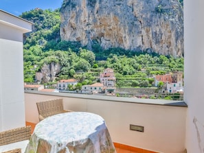 Un balcón con mobiliario de mimbre y una mesa, con vista a un pueblo con edificios y un acantilado.