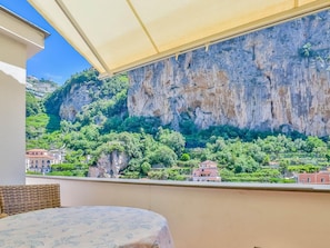 Un balcón con vista a un acantilado y follaje, una mesa y una silla de mimbre.