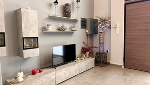 A modern living room with a flat-screen TV, built-in shelves, decorative items, and a large potted plant. - Thissio Luxury Apartment (Athens)