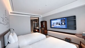 Una habitación de hotel moderna con una cama grande, un televisor montado en la pared, una mesita de noche y un armario.