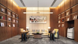 Eine moderne Lobby mit einer Couch, Sesseln, einem Couchtisch und einem Bücherregal.