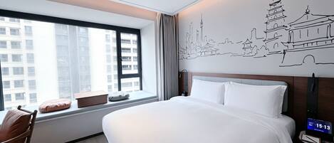 A hotel room with a large bed, a chair, a window with a city view, and a wall with a cityscape mural.