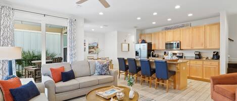 A spacious living room with a sofa, coffee table, and a dining area with chairs and a kitchen in the background.
