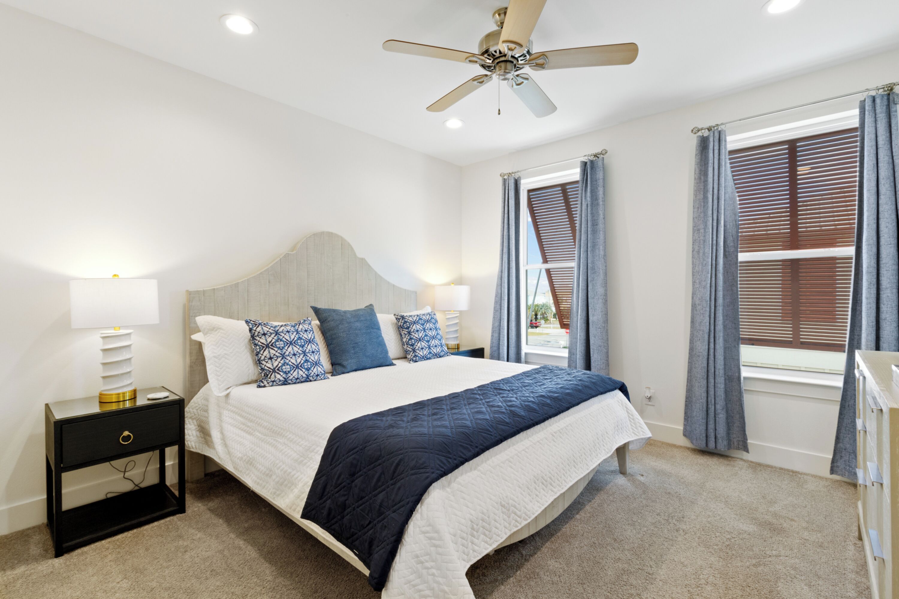 A bedroom with a bed, nightstand, lamp, ceiling fan, and window with curtains.