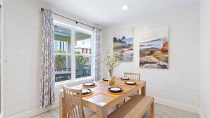 A dining area with a wooden table set for four, a vase with flowers, and two paintings on the wall. - Drift Away (Gulf Shores)
