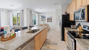 A modern kitchen with granite countertops, stainless steel appliances, wooden cabinets, and a large island. - Drift Away (Gulf Shores)