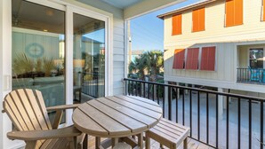 A balcony with a wooden table and two chairs, overlooking a building with orange shutters. - Drift Away (Gulf Shores)