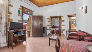 A living room with a television on a wooden stand, a fireplace, a sofa, and a dining table. - Countryside Apartment 2 With Shared Swimming Pool (Kissamos)