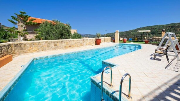A swimming pool with clear blue water, surrounded by a stone wall and a tiled deck. - Countryside Apartment 2 With Shared Swimming Pool (Kissamos)
