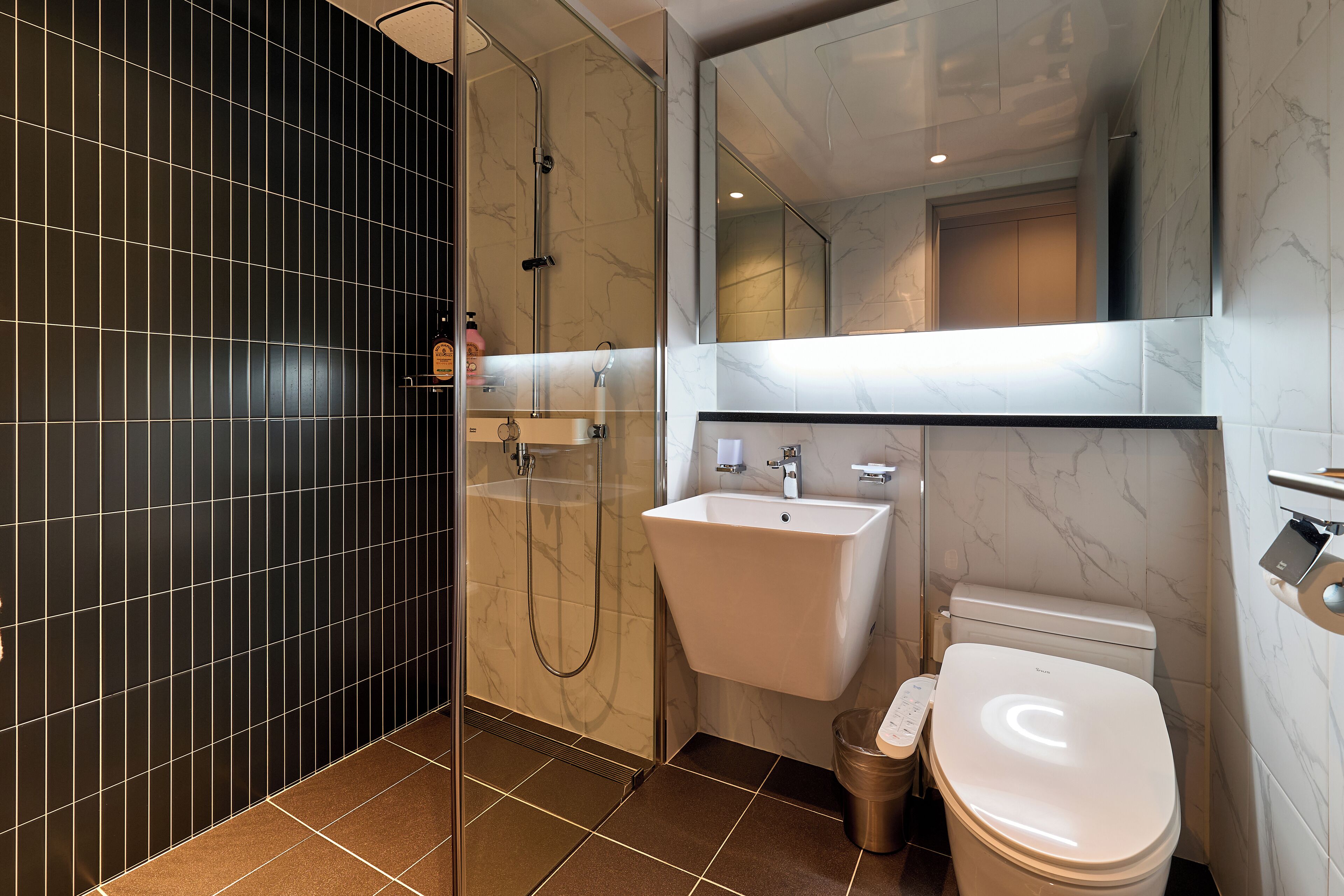Een moderne badkamer met een douche met glazen wand, een wit wastafeltje en een toilet.