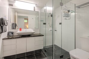 A modern bathroom with a glass-enclosed shower, a white sink, and a large mirror.