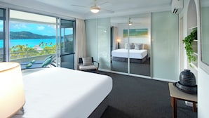 Ett hotellrum med en stor säng, en stol, ett bord och utsikt över havet.