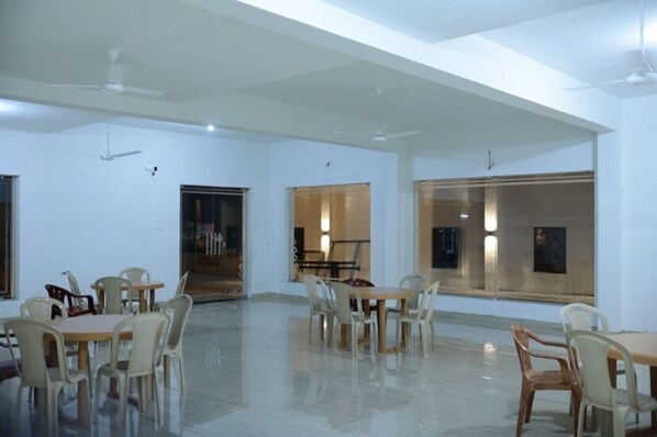 A spacious room with multiple tables and chairs, large windows, and ceiling fans.