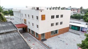A modern hotel with a flat roof, a red awning, and a sign with a crown symbol. - RRR Grand by Prince Resorts- Experience Luxury in a Natural Embrace (Perundurai)