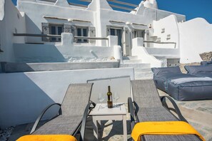 A terrace with white-washed buildings, a table with a bottle and glass, and lounge chairs. - Apleton Villas Paros (Paros)