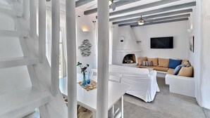 A modern living room with a white sofa, a dining table with a vase, and a fireplace. - Apleton Villas Paros (Paros)