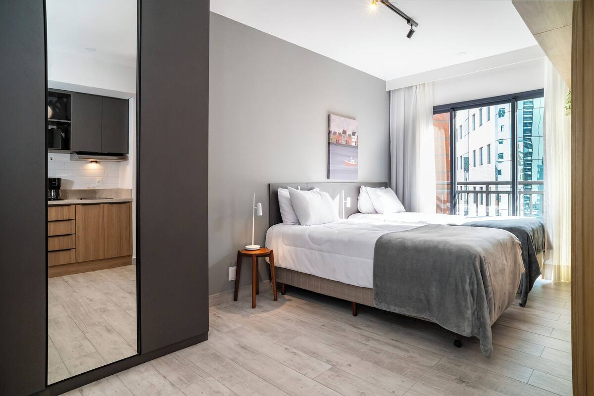 A modern bedroom with a large bed, a bedside table, and a view of the city through a large window.