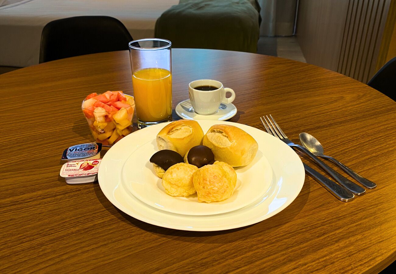 Een ontbijttafel met gebak, een glas sinaasappelsap, een kop koffie en een klein bakje yoghurt.
