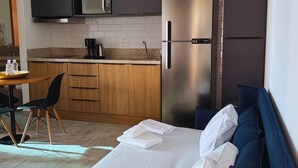 A compact hotel room with a bed, a small kitchenette, a dining area, and a bathroom.