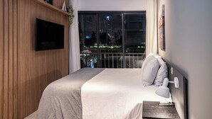 A modern hotel room with a large bed, a mounted TV, and a balcony with a city view.