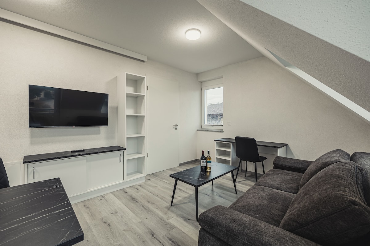 A modern living space with a flat-screen TV, a dining table, a sofa, and a small kitchen area.