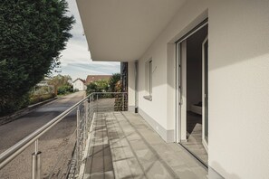 Un immeuble résidentiel doté d’un balcon, d’un chemin pavé et offrant une vue dégagée sur la rue et les maisons voisines.