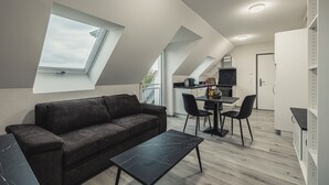 Egy modern, galériaszerű lakás, amelyben étkező, kis konyha található, és egy nagy ablak biztosítja a természetes fényt.