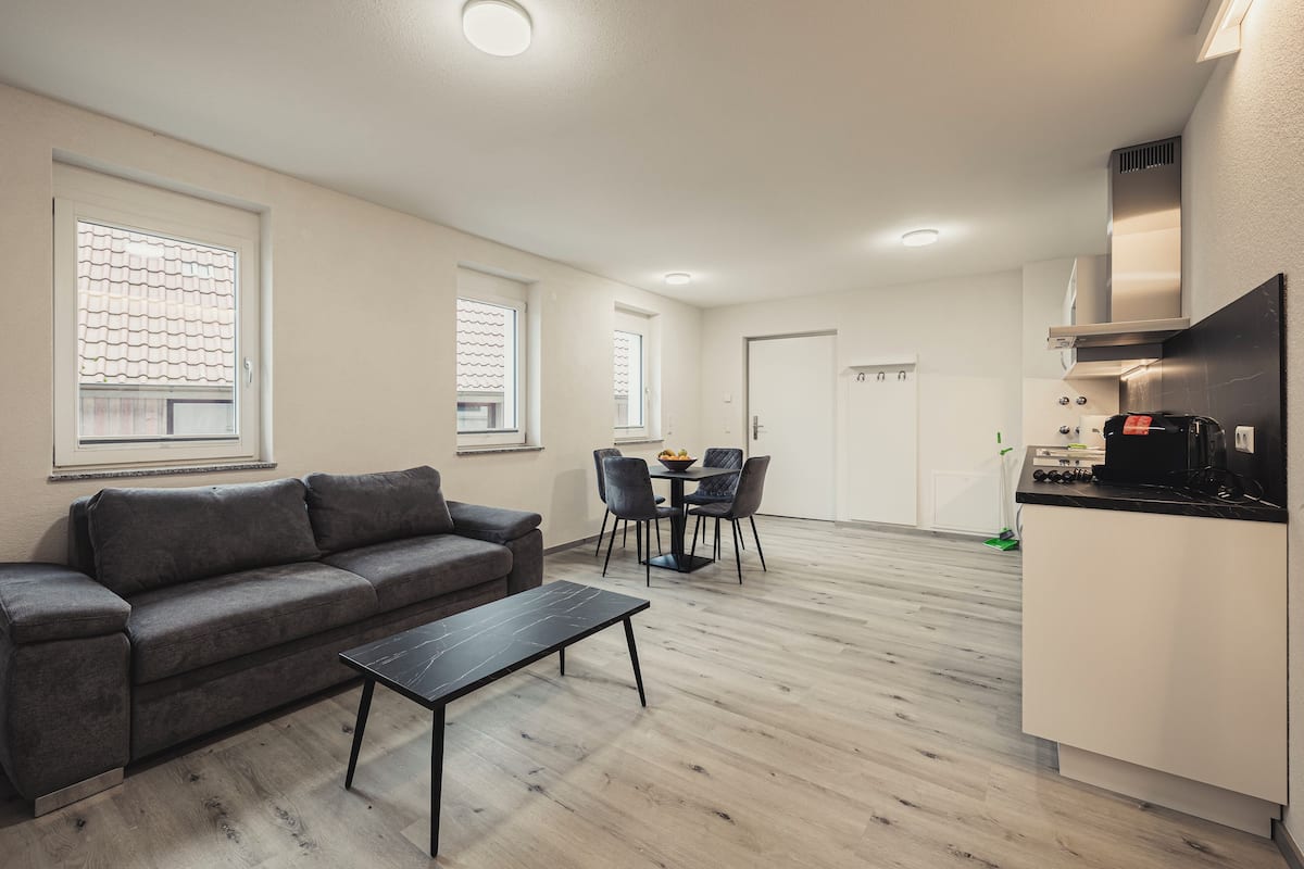 A modern living room with a grey sofa, a black coffee table, and a dining area with a table and chairs.