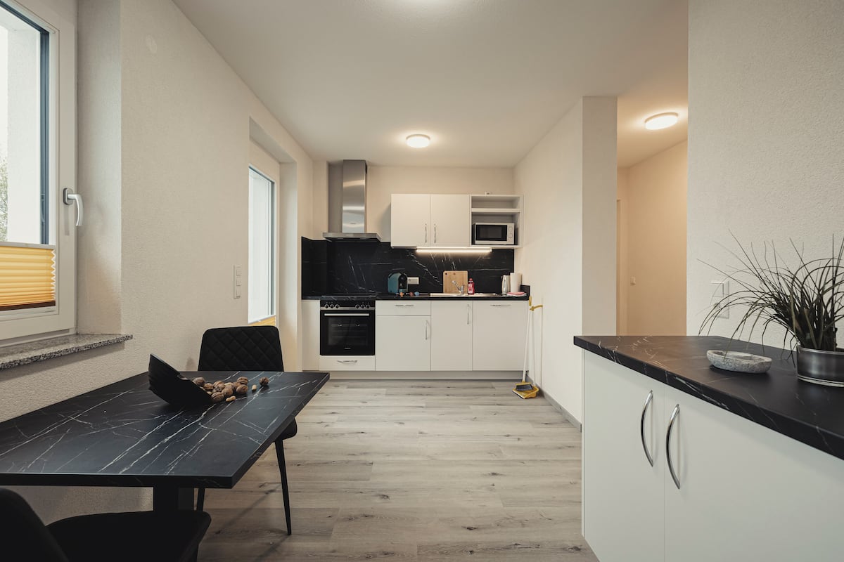 A compact kitchen with white cabinets, a black countertop, and a dining area with a table and chairs.