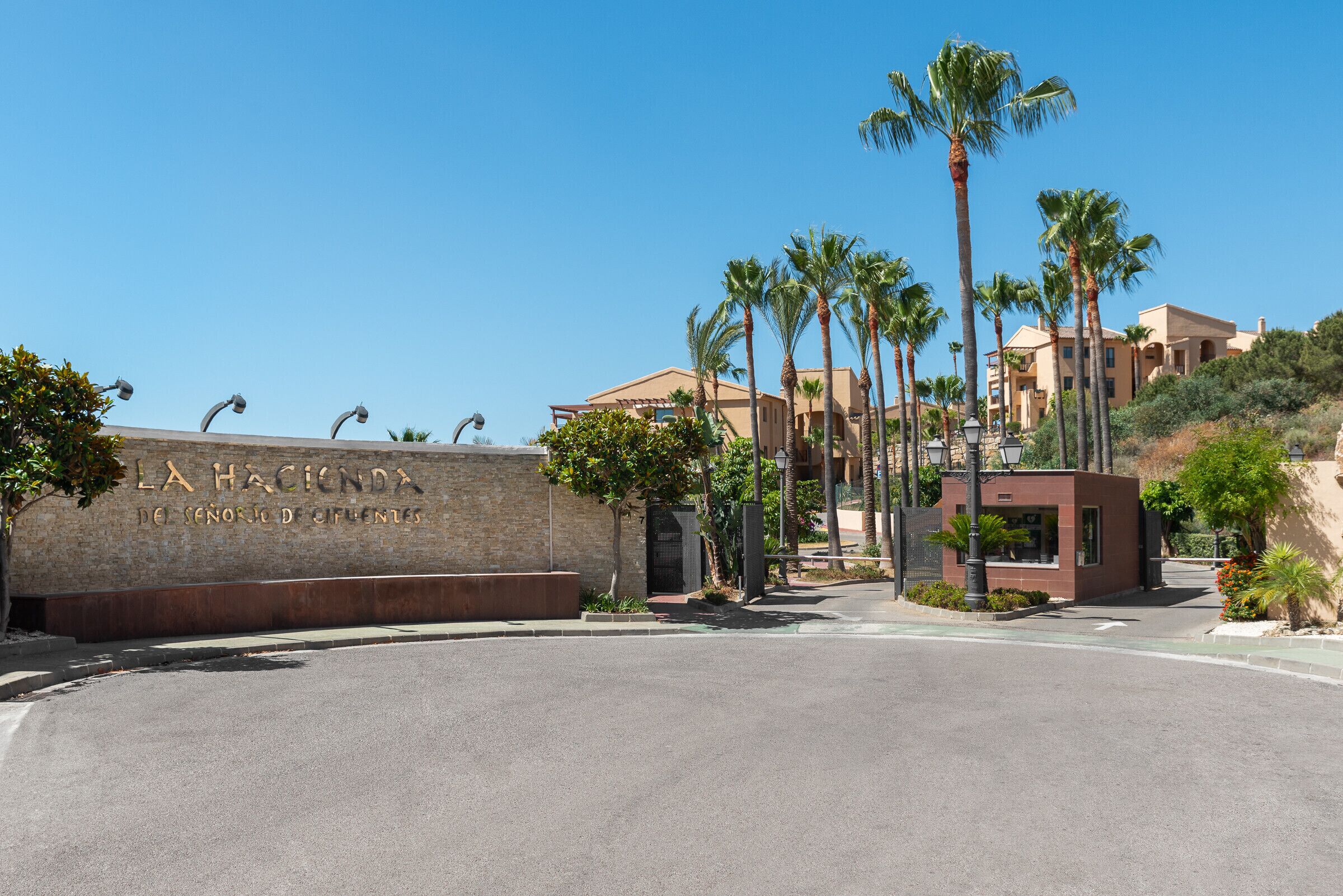A hotel entrance with a prominent sign, palm trees, and a clear sky.