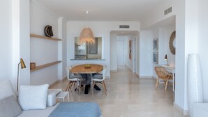 Ein modernes Wohnzimmer mit einer Couch, einem Esstisch mit Stühlen, einer Hängelampe und einer Küchenzeile im Hintergrund.