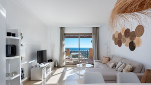 A modern living room with a sofa, coffee table, and TV, leading to a balcony with a view of the sea. - Premium Penthouse with Unmatched Views (Benahavís)