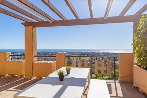 A balcony with a white table and chairs, a potted plant, and a view of the sea and cityscape. - Premium Penthouse with Unmatched Views (Benahavís)