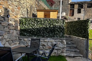 Un muro de piedra con un banco de madera y una mesa, una escalera de piedra y un seto.