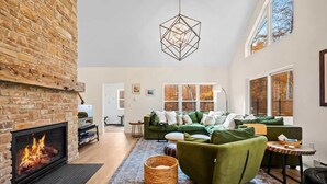 A spacious living room with a fireplace, green sofas, a woven basket, and a geometric pendant light. - Pet-Friendly Modern Retreat · Woods · Ellison Bay (Ellison Bay)