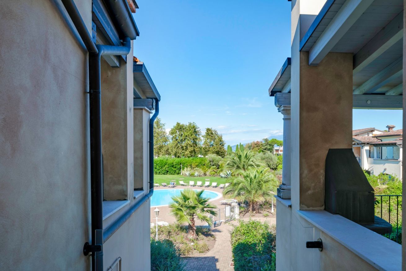 A view from a balcony overlooking a swimming pool, palm trees, and a garden.