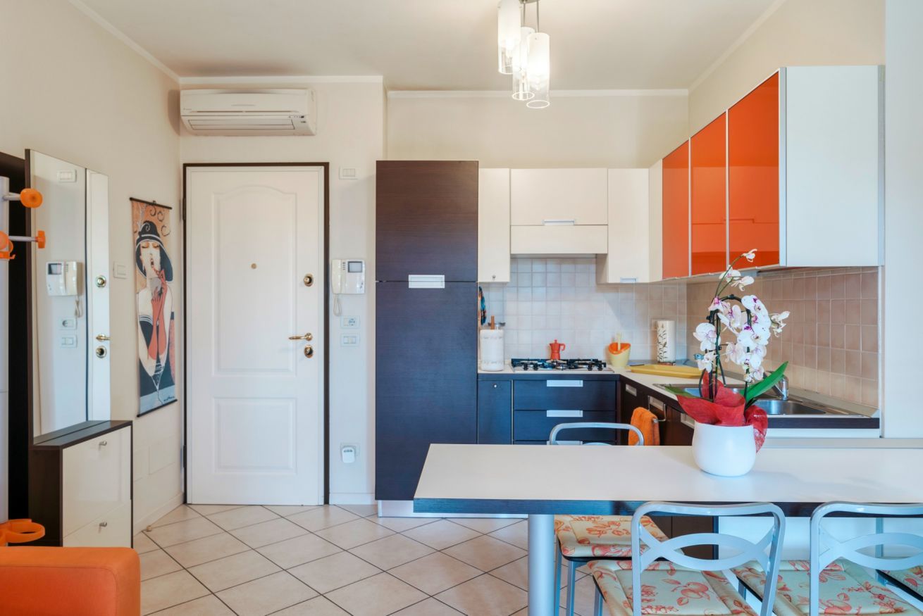 Une cuisine moderne avec des meubles blancs et orange, un plan de travail blanc et un coin repas comprenant une table et des chaises.