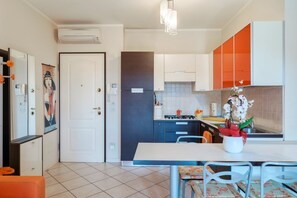 A modern kitchen with white and orange cabinets, a white countertop, and a dining area with a table and chairs. - Sisy by the Lake—with Wi-Fi, a pool, and a garage (Sirmione)
