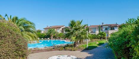 A pool area with a circular stone design, surrounded by greenery and buildings with tiled roofs.